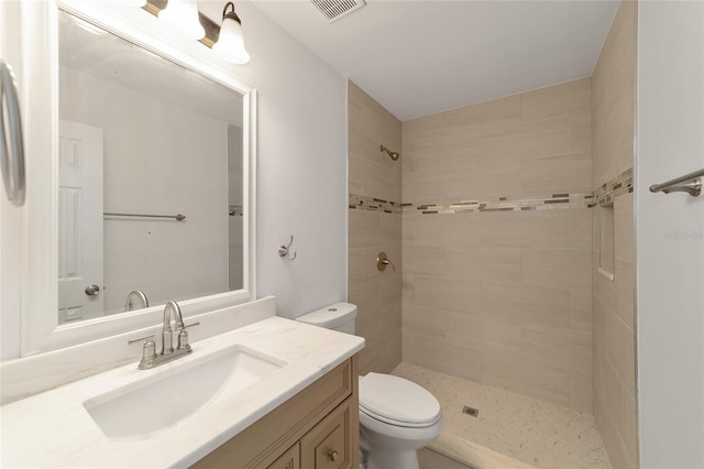 bathroom featuring toilet, a tile shower, and vanity
