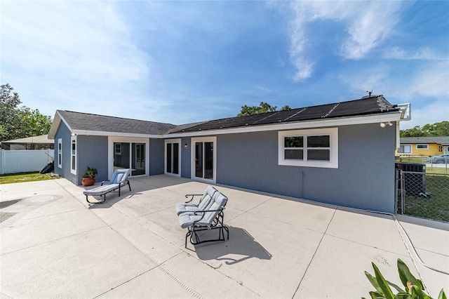 back of property featuring fence, a patio area, and roof mounted solar panels