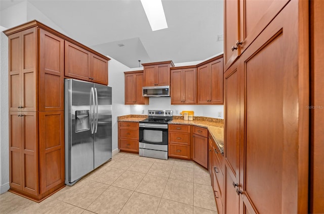 kitchen with lofted ceiling with skylight, light tile patterned floors, light stone countertops, and appliances with stainless steel finishes