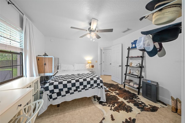 bedroom featuring ceiling fan, light tile patterned floors, and a textured ceiling