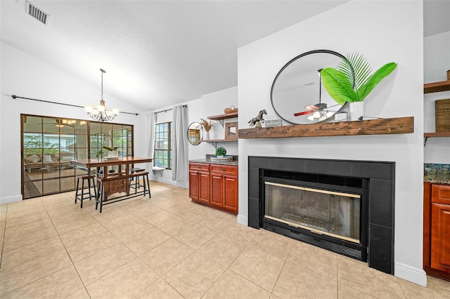 living room with ceiling fan with notable chandelier, a fireplace, light tile patterned floors, and vaulted ceiling