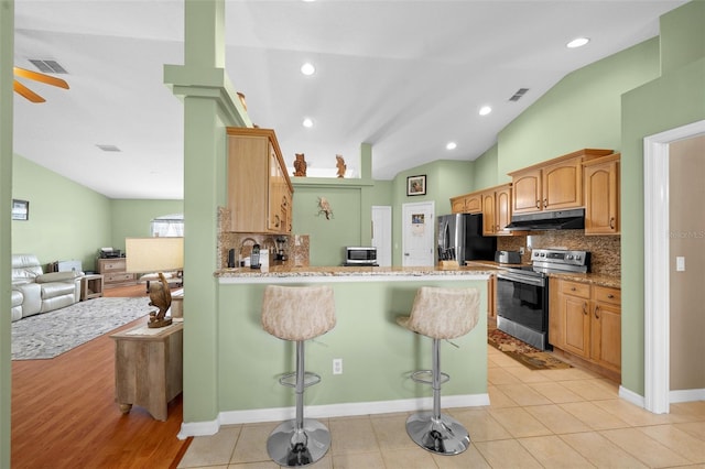 kitchen with vaulted ceiling, appliances with stainless steel finishes, kitchen peninsula, a kitchen breakfast bar, and decorative backsplash