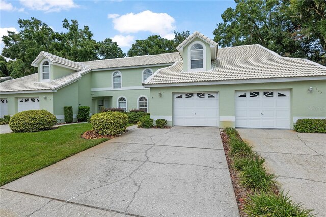 view of front facade featuring a tile roof, an attached garage, a front yard, and stucco siding