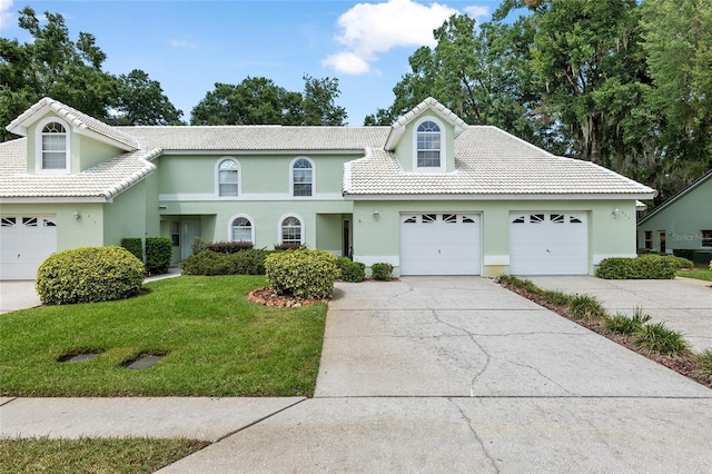 view of front of property with a tiled roof, driveway, an attached garage, and a front yard