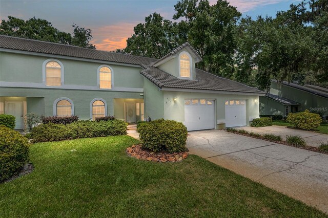 view of front of property with a tiled roof, concrete driveway, a front yard, stucco siding, and a garage