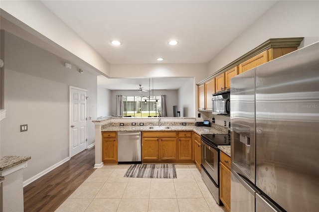 kitchen featuring light stone countertops, light hardwood / wood-style floors, hanging light fixtures, stainless steel appliances, and kitchen peninsula