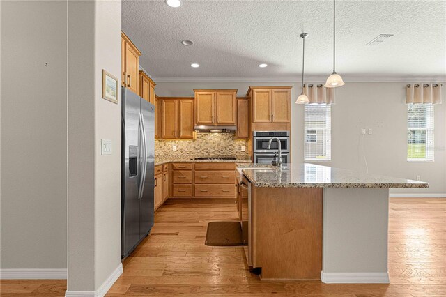 kitchen featuring light stone counters, tasteful backsplash, appliances with stainless steel finishes, light wood-type flooring, and under cabinet range hood