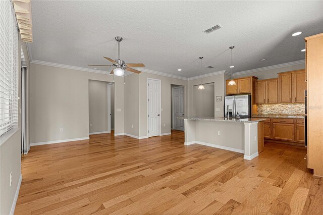 kitchen featuring stainless steel refrigerator with ice dispenser, decorative backsplash, ceiling fan, ornamental molding, and an island with sink