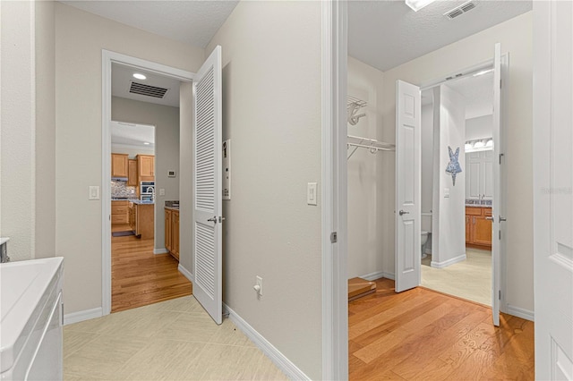 corridor featuring light wood finished floors, baseboards, and visible vents