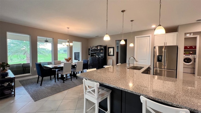 kitchen with light stone counters, sink, washer / dryer, pendant lighting, and stainless steel fridge with ice dispenser