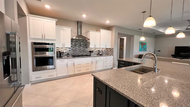 kitchen featuring pendant lighting, stainless steel appliances, sink, white cabinetry, and wall chimney range hood