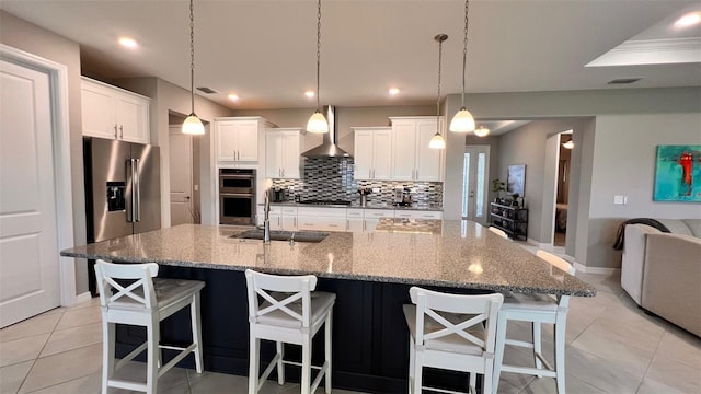 kitchen with appliances with stainless steel finishes, a large island with sink, sink, wall chimney range hood, and a breakfast bar area