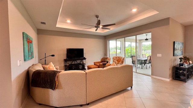 tiled living room with ceiling fan, ornamental molding, and a tray ceiling