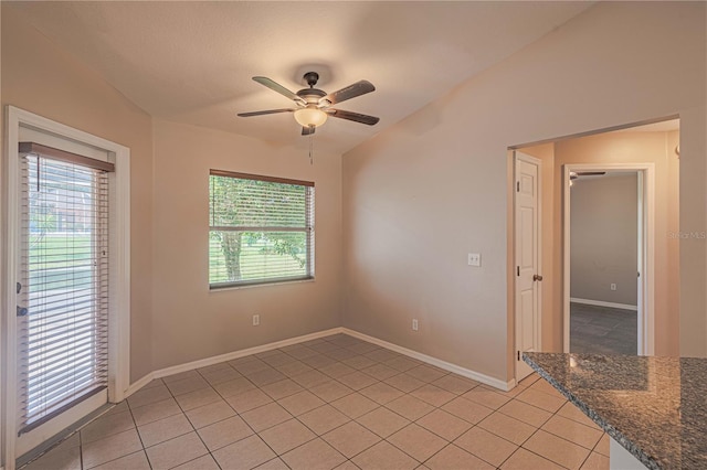 empty room with lofted ceiling, light tile patterned floors, baseboards, and a ceiling fan