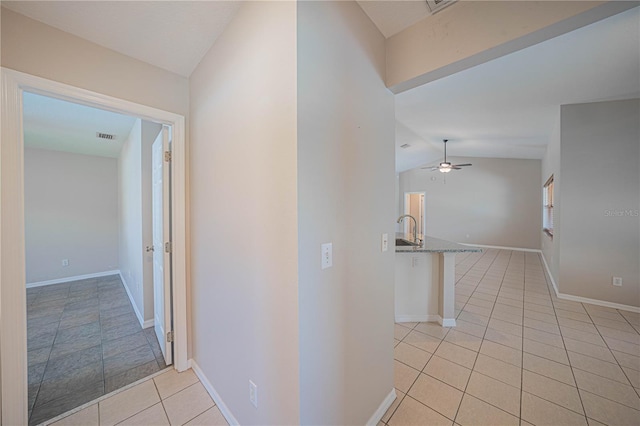 hallway with light tile patterned floors, visible vents, vaulted ceiling, a sink, and baseboards