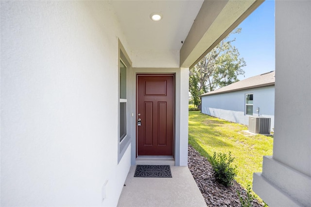 view of exterior entry with a lawn and central AC