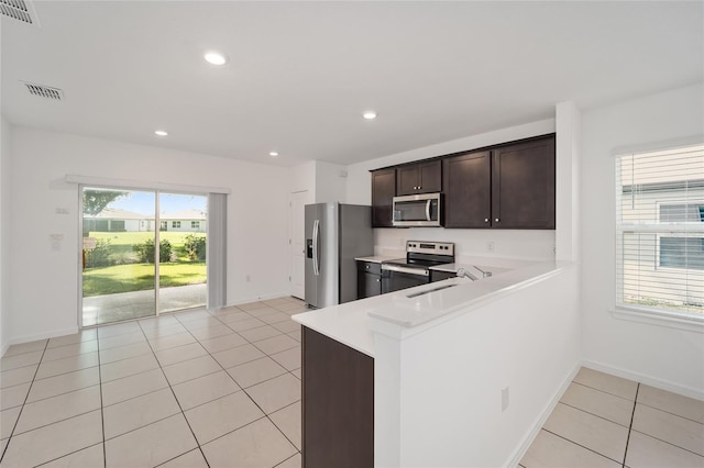 kitchen with appliances with stainless steel finishes, light tile patterned flooring, kitchen peninsula, dark brown cabinetry, and sink