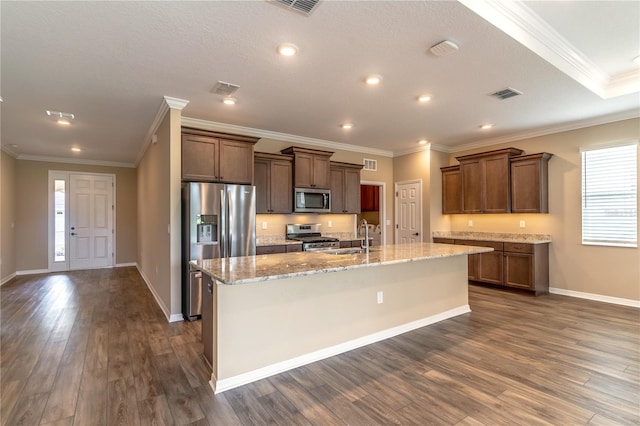 kitchen with light stone counters, a sink, appliances with stainless steel finishes, dark wood-style floors, and a center island with sink