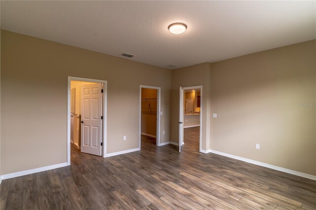 unfurnished bedroom featuring dark wood-style floors, a walk in closet, a closet, visible vents, and baseboards