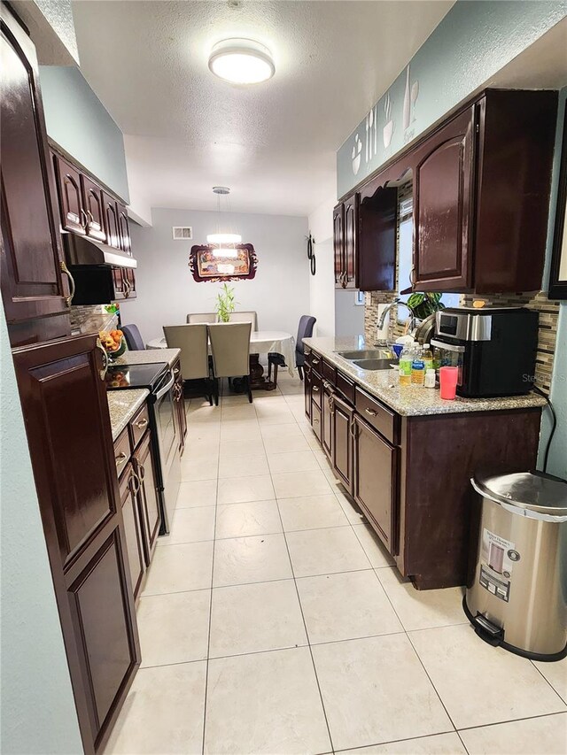 kitchen with a textured ceiling, light stone countertops, hanging light fixtures, sink, and electric stove