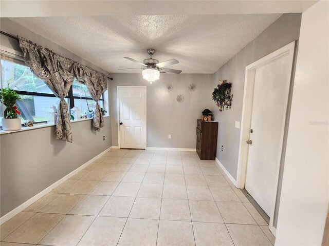 empty room featuring a textured ceiling, light tile patterned flooring, and ceiling fan