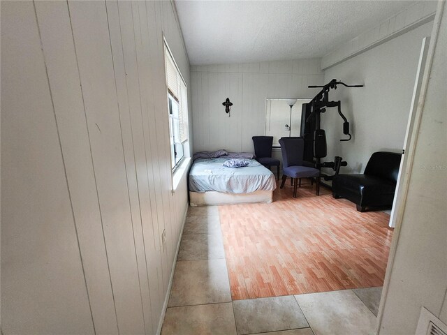 bedroom with wooden walls, light hardwood / wood-style floors, and a textured ceiling