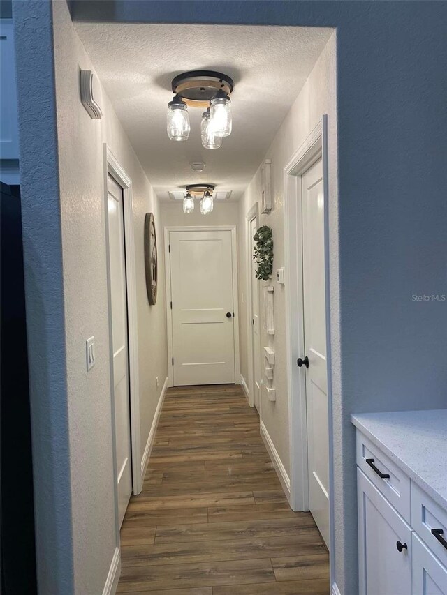 corridor with a textured ceiling and dark wood-type flooring