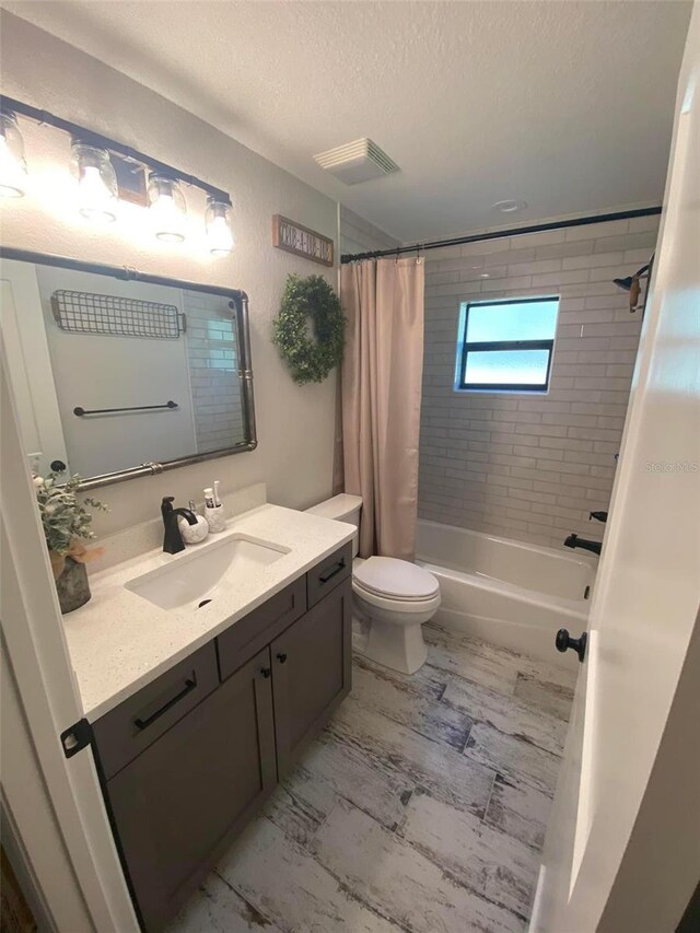 full bathroom featuring shower / bath combo with shower curtain, a textured ceiling, vanity, and toilet