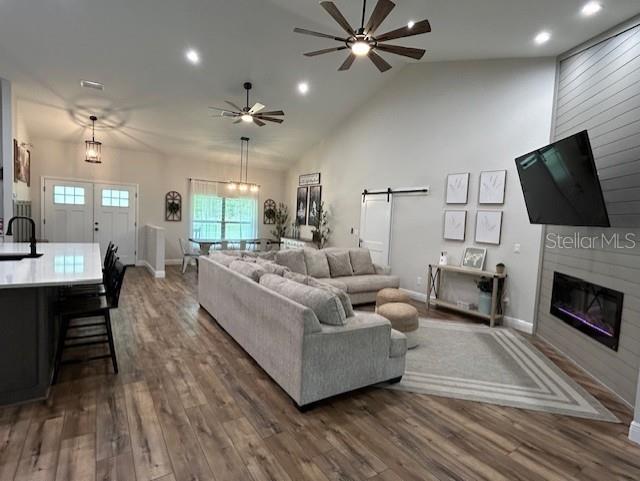 living room with ceiling fan with notable chandelier, vaulted ceiling, dark hardwood / wood-style floors, and a barn door