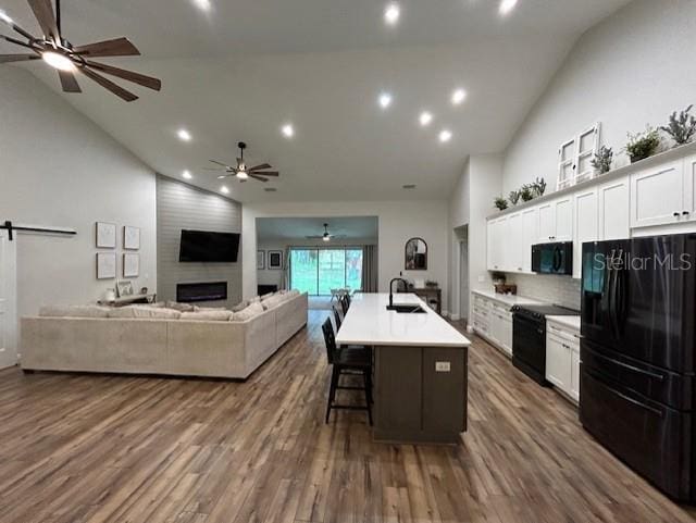 kitchen featuring an island with sink, white cabinets, dark hardwood / wood-style flooring, black appliances, and ceiling fan