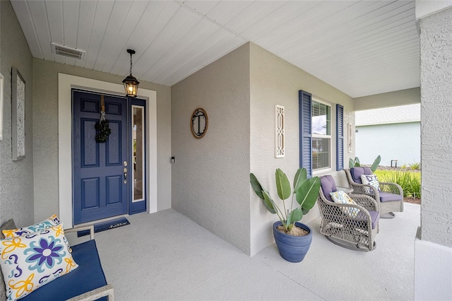 view of exterior entry with covered porch, visible vents, and stucco siding