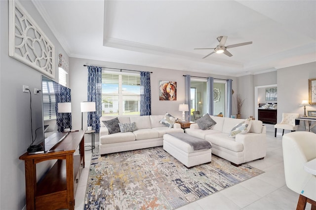 living room with a ceiling fan, a tray ceiling, crown molding, and light tile patterned floors