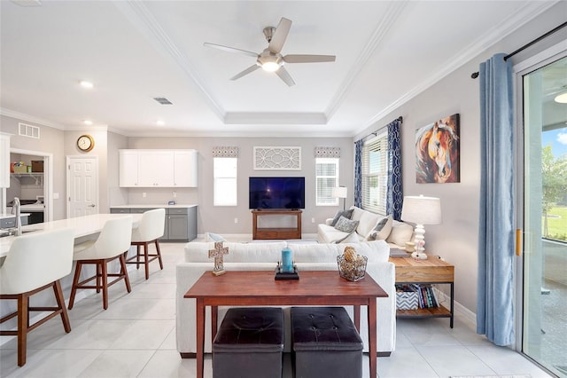 living area with light tile patterned floors, a ceiling fan, baseboards, a tray ceiling, and crown molding