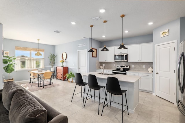 kitchen with appliances with stainless steel finishes, pendant lighting, white cabinetry, an island with sink, and sink