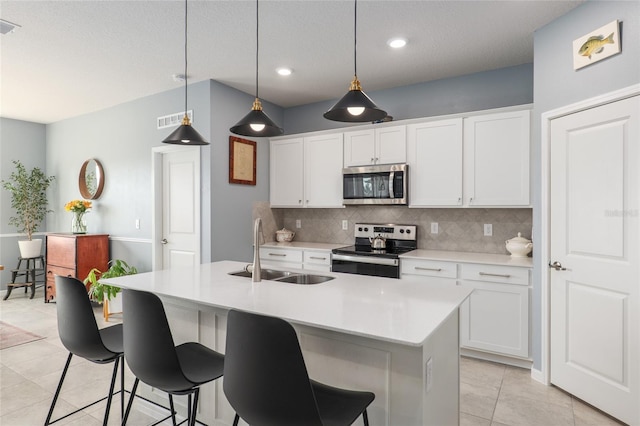 kitchen with appliances with stainless steel finishes, white cabinetry, sink, hanging light fixtures, and a kitchen island with sink