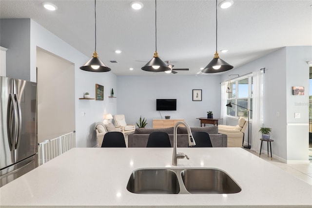 kitchen with sink, decorative light fixtures, a textured ceiling, stainless steel fridge, and light stone countertops