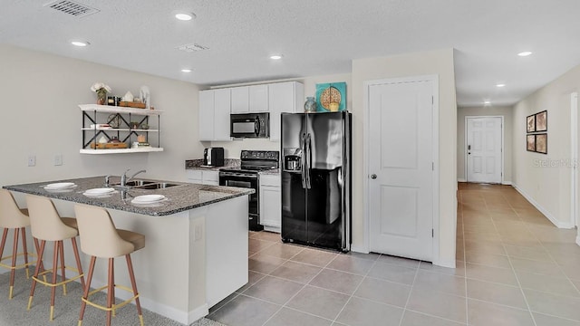 kitchen featuring a kitchen island with sink, a textured ceiling, black appliances, sink, and white cabinets