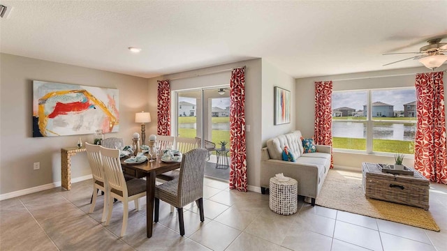 tiled dining room with ceiling fan, a textured ceiling, a water view, visible vents, and baseboards