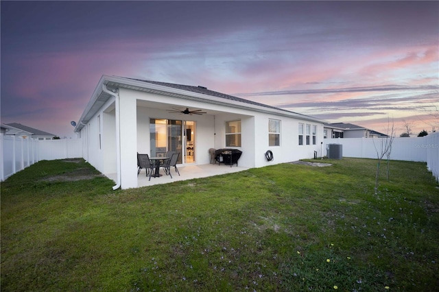 back house at dusk featuring a yard, ceiling fan, a patio, and central AC