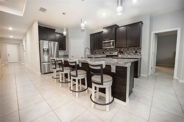 kitchen with decorative light fixtures, appliances with stainless steel finishes, a kitchen island with sink, a breakfast bar, and decorative backsplash