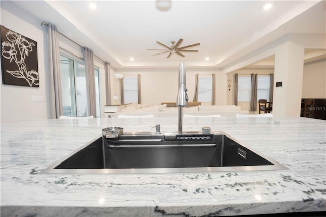 kitchen with a tray ceiling, ceiling fan, light stone countertops, and sink