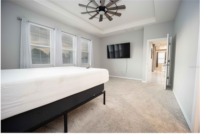 bedroom with a tray ceiling, light carpet, and ceiling fan