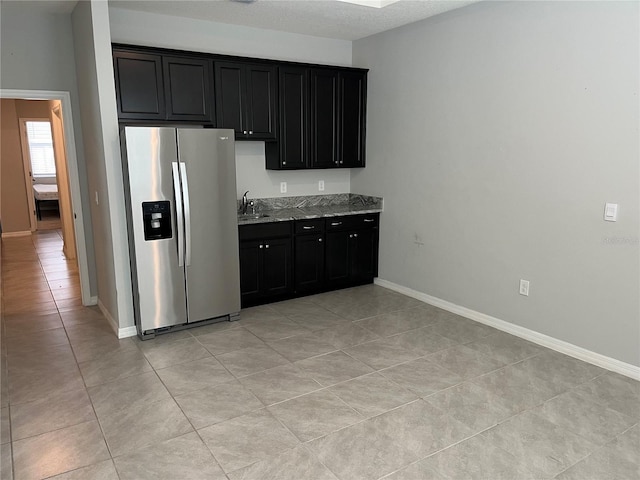 kitchen with light tile patterned floors, light stone counters, sink, stainless steel fridge with ice dispenser, and a textured ceiling