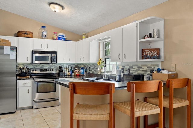 kitchen featuring lofted ceiling, a sink, white cabinets, appliances with stainless steel finishes, and dark countertops