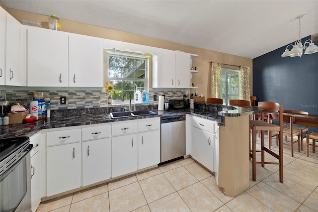 kitchen featuring a peninsula, a sink, white cabinets, stainless steel dishwasher, and decorative backsplash