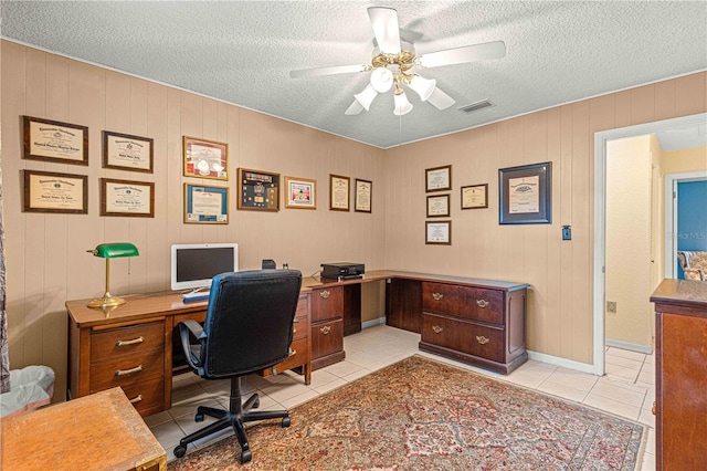 tiled home office with ceiling fan, wooden walls, and a textured ceiling