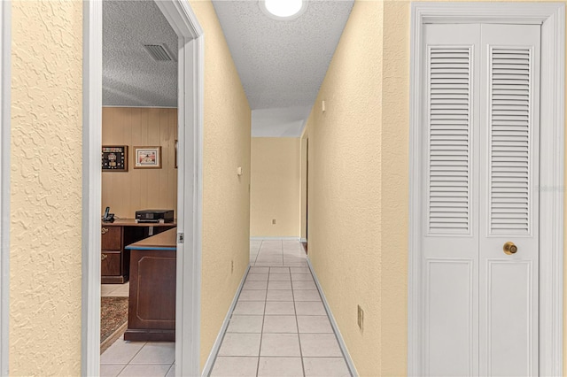 hall featuring a textured ceiling, light tile patterned floors, and wooden walls