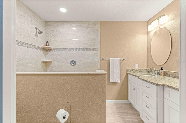 bathroom with a textured ceiling, vanity, and a tile shower