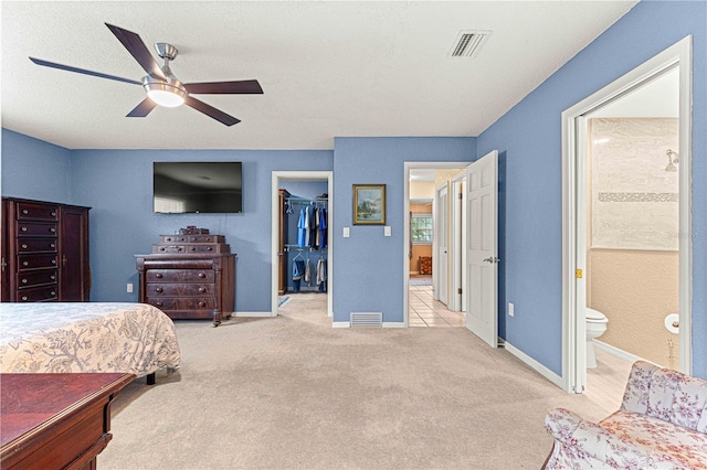 carpeted bedroom with a textured ceiling, a walk in closet, a closet, ensuite bath, and ceiling fan