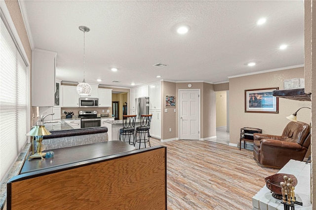 kitchen with appliances with stainless steel finishes, light hardwood / wood-style floors, ornamental molding, sink, and white cabinets